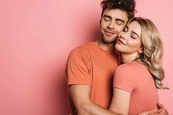 Feliz jovem casal abraçando com olhos fechados no fundo rosa — Fotografia de Stock