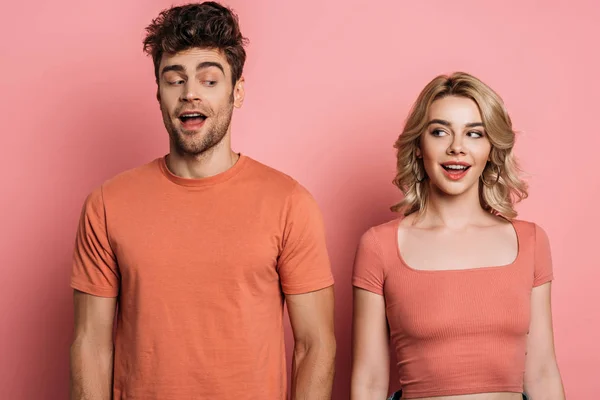 Positive, tricky man and woman looking at each other on pink background — Stock Photo