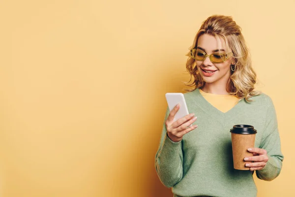 Lächelndes Mädchen, das auf dem Smartphone chattet und Kaffee hält, um auf gelbem Hintergrund zu gehen — Stockfoto