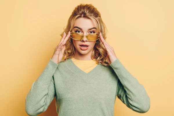 Attraktives, selbstbewusstes Mädchen, das eine Brille berührt, während es in die Kamera auf gelbem Hintergrund blickt — Stockfoto