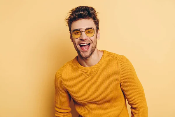 Handsome man in glasses laughing at camera on yellow background — Stock Photo