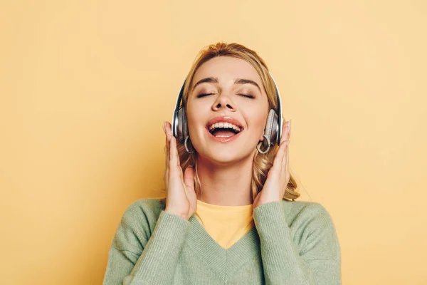 Happy girl listening music in wireless headphones with closed eyes on yellow background — Stock Photo