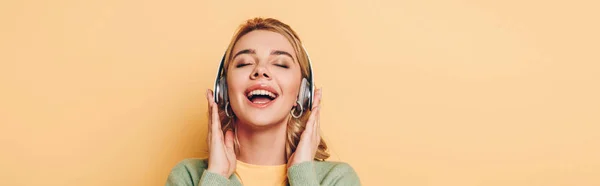 Panoramic shot of happy girl listening music in wireless headphones with closed eyes on yellow background — Stock Photo