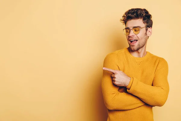 Fröhlicher junger Mann, der mit dem Finger zeigt, während er auf gelbem Hintergrund wegschaut — Stockfoto
