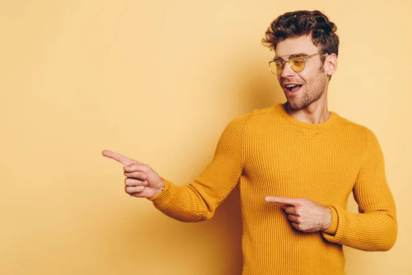 Hombre positivo señalando con los dedos mientras mira hacia otro lado sobre fondo amarillo - foto de stock