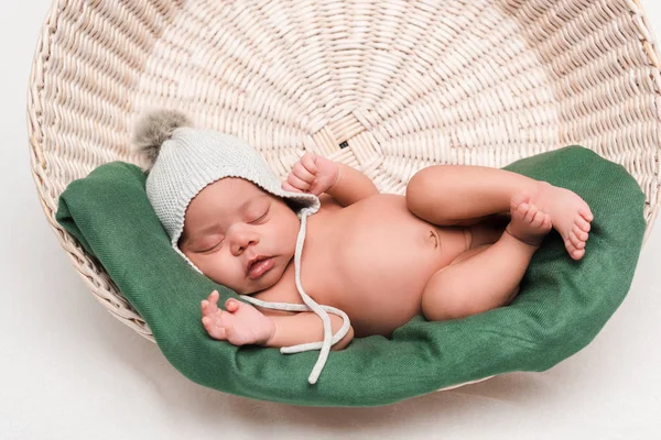 Новорожденный ребенок смешанной расы в трикотажной шляпе спит в корзине на белом — стоковое фото