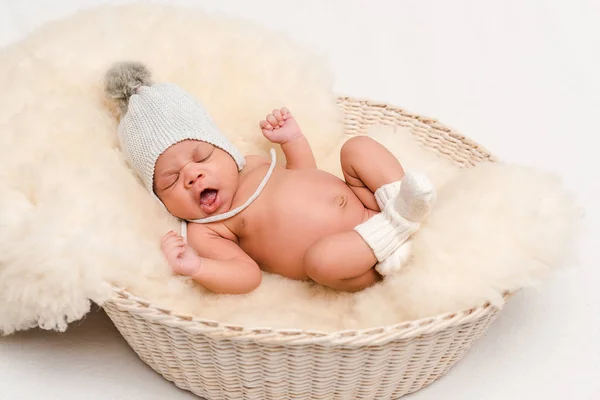 Nouveau-né mélange race bébé en bonnet tricoté bâillement dans le panier sur blanc — Photo de stock