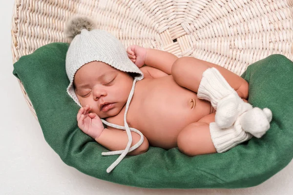 Newborn mixed race baby in knitted hat and socks sleeping in basket on white — Stock Photo