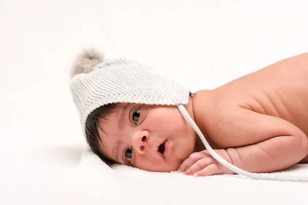 Cute bi-racial newborn baby in knitted hat lying on white — Stock Photo