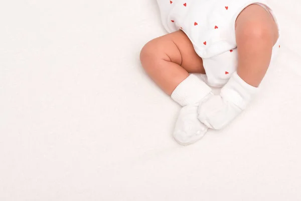 Recortado vista de lindo recién nacido en bebé mameluco y calcetines acostado aislado en blanco - foto de stock