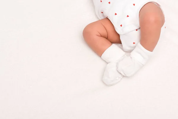 Recortado vista de lindo recién nacido en bebé mameluco y calcetines acostado aislado en blanco - foto de stock