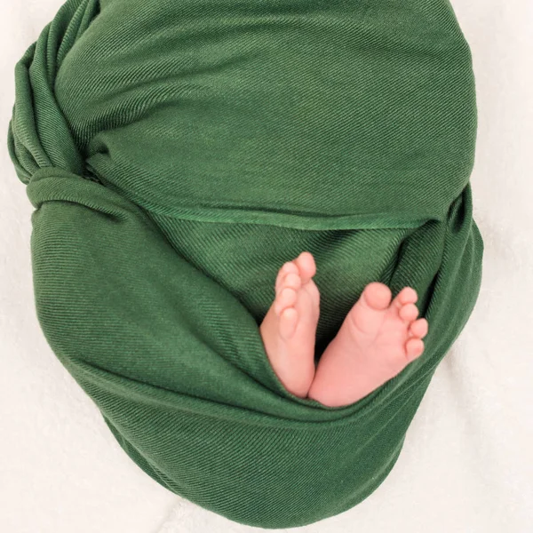 Обрезанный вид ребенка, завернутого в зеленое одеяло, лежащего на белом — стоковое фото
