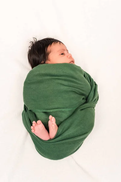 Blick von oben auf ein Baby, das in eine grüne Decke gehüllt auf weißem Grund liegt — Stockfoto