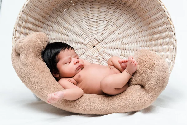 Desnudo mezclado raza bebé durmiendo en cesta en blanco - foto de stock