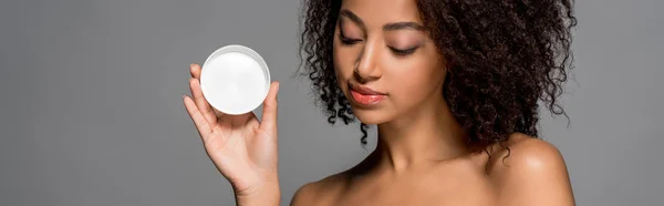Panoramic shot of african american girl holding plastic container with cosmetic cream, isolated on grey — Stock Photo
