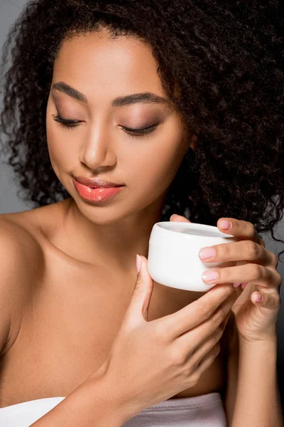 Menina americana africana feliz segurando creme anti-rugas, isolado em cinza — Fotografia de Stock