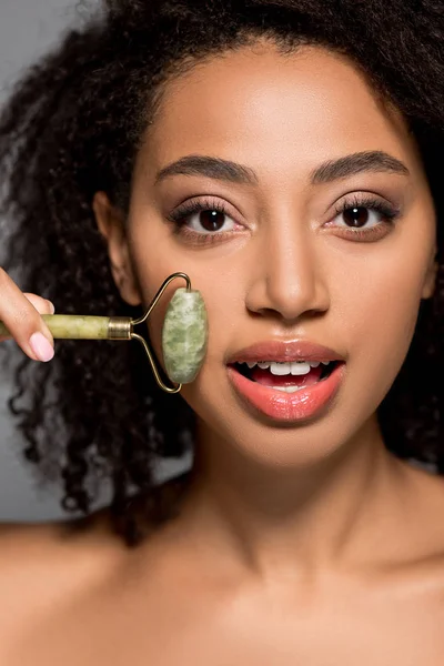 Souriant afro-américaine fille à l'aide de rouleau de jade, isolé sur gris — Photo de stock