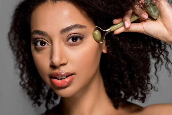 Portrait de fille afro-américaine utilisant un rouleau de jade, isolé sur gris — Photo de stock