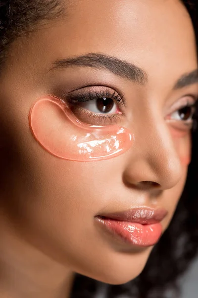 Beautiful african american girl with hydrogel eye patches, on grey — Stock Photo
