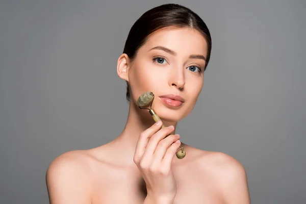 Linda menina nua usando rolo de massagem jade, isolado em cinza — Fotografia de Stock