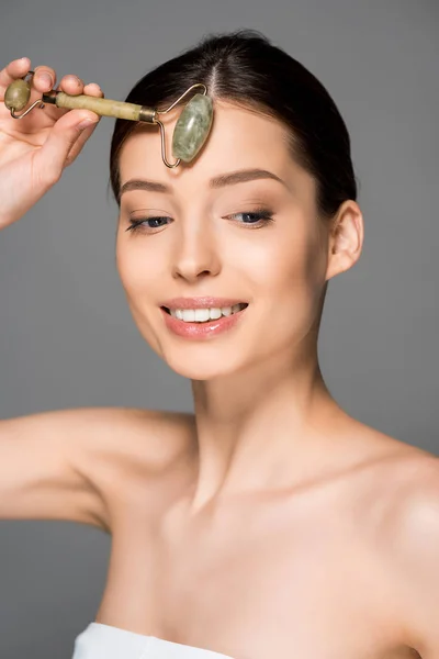 Beautiful smiling woman using jade roller, isolated on grey — Stock Photo