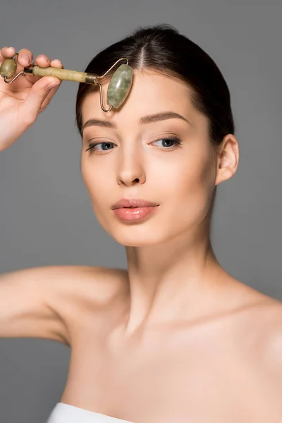 Beautiful woman using jade roller, isolated on grey — Stock Photo