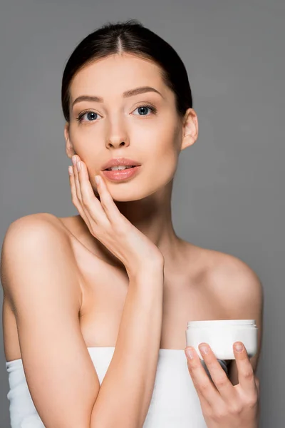 Beautiful tender girl applying face cream, isolated on grey — Stock Photo