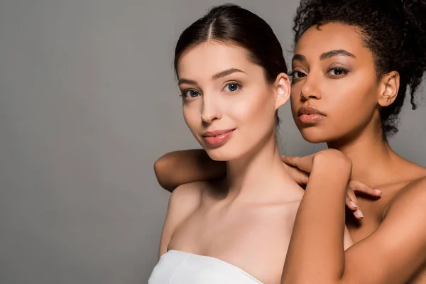 Retrato de atractivas mujeres multiétnicas sonrientes con caras limpias, aisladas en gris — Stock Photo