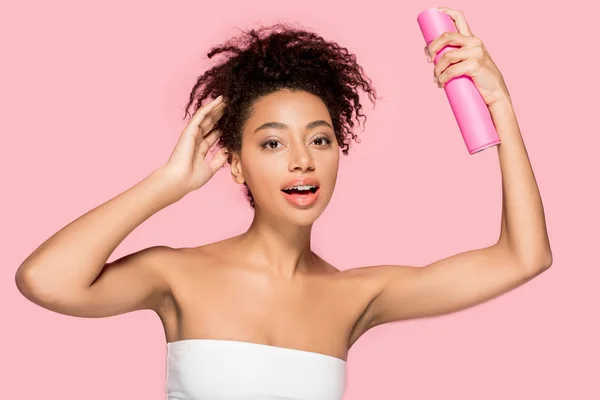 Menina americana africana atraente com garrafa de spray de cabelo, isolado em rosa — Fotografia de Stock