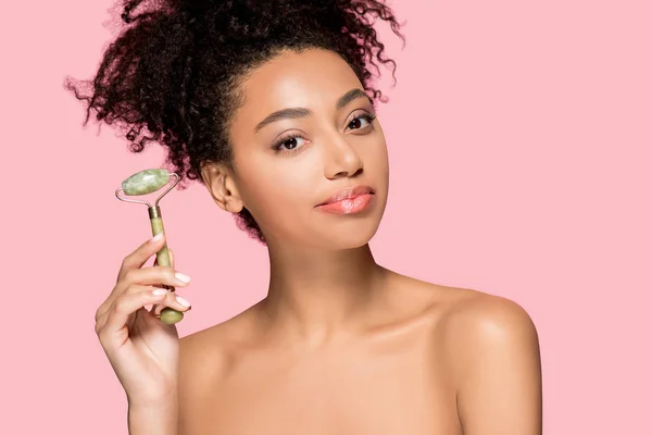 Beautiful naked african american girl using jade roller, isolated on pink — Stock Photo