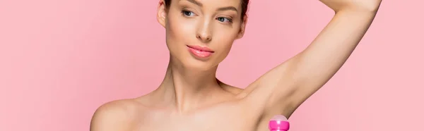 Panoramic shot of beautiful girl applying roll deodorant, isolated on pink — Stock Photo