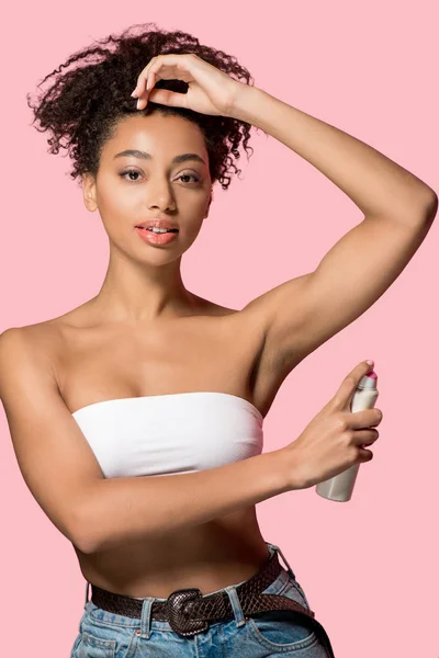 Atractiva chica afroamericana usando desodorante spray, aislado en rosa - foto de stock