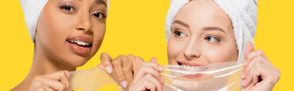 Panoramic shot of smiling multiracial girls holding hydrogel masks, isolated on yellow — Stock Photo