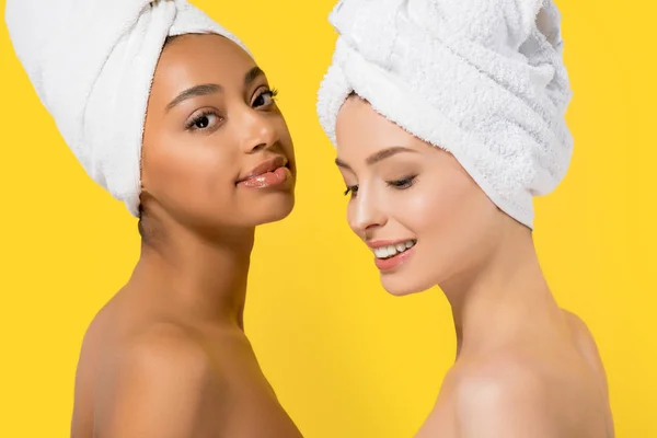 Cheerful multicultural girls with towels on heads, isolated on yellow — Stock Photo
