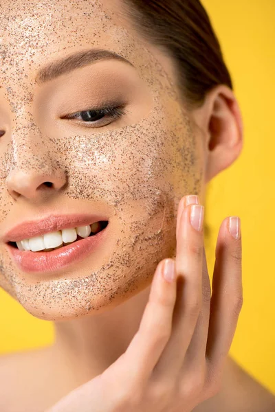 Portrait of smiling girl applying peeling mask, isolated on yellow — Stock Photo