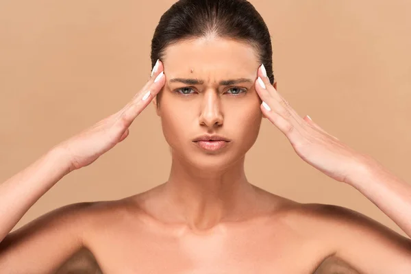 Femme concentrée et nue avec bouton sur les tempes touchantes du visage isolé sur beige — Photo de stock