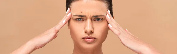 Panoramic shot of focused woman with pimple on face touching temples isolated on beige — Stock Photo