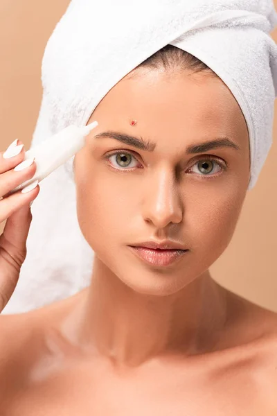 Naked woman in towel holding treatment cream near face with problem skin isolated on beige — Stock Photo