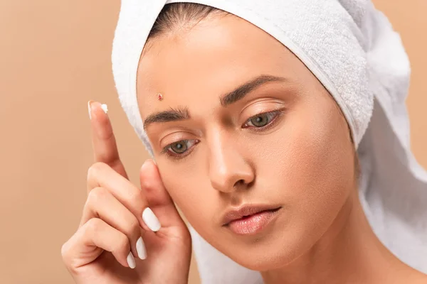 Jeune femme en serviette avec crème de traitement sur doigt isolé sur beige — Photo de stock