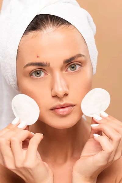 Young woman with pimple on face holding cotton pads isolated on beige — Stock Photo