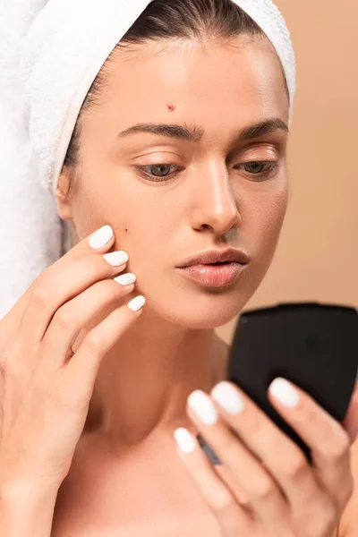 Foyer sélectif de la femme touchant le visage avec des boutons et regardant le miroir isolé sur beige — Photo de stock