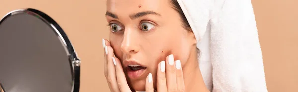 Panoramic shot of surprised girl touching face with pimples and looking at mirror isolated on beige — Stock Photo