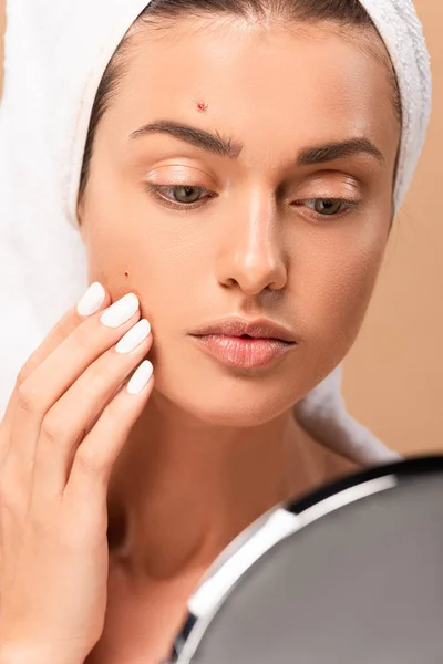 Foyer sélectif de la fille dans la serviette toucher le visage avec des boutons et en regardant miroir isolé sur beige — Photo de stock