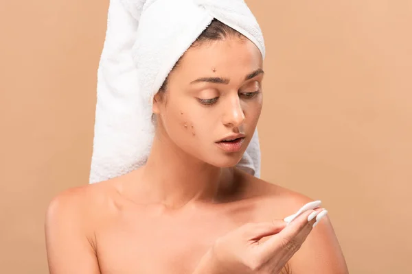 Young naked woman in towel looking at cotton pad isolated on beige — Stock Photo