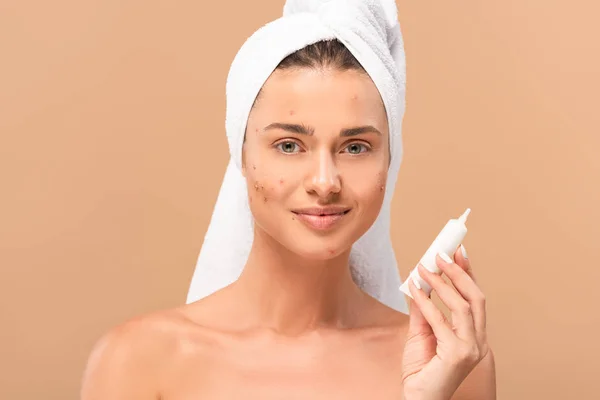 Felice e nuda ragazza con acne sul viso crema di trattamento tenuta isolato su beige — Foto stock
