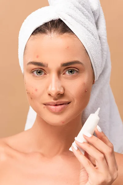 Menina alegre e nua com acne no rosto segurando creme de tratamento isolado no bege — Fotografia de Stock