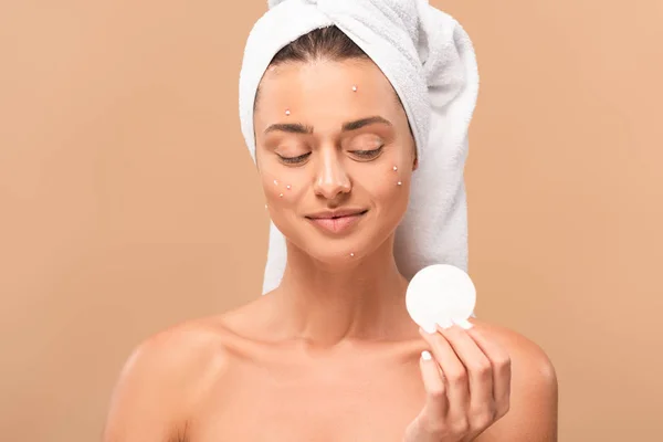 Smiling naked girl with acne on face looking at cotton pad isolated on beige — Stock Photo