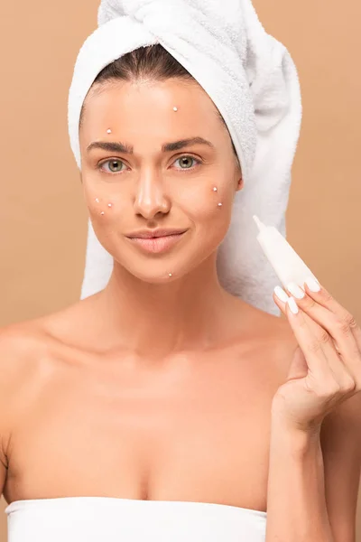 Menina sorridente com acne no rosto segurando creme de tratamento isolado no bege — Fotografia de Stock