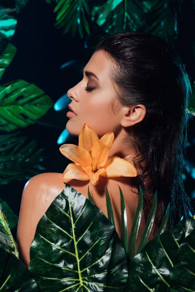 Vue latérale de la jeune femme nue près de l'orchidée en fleurs et des feuilles vertes — Photo de stock