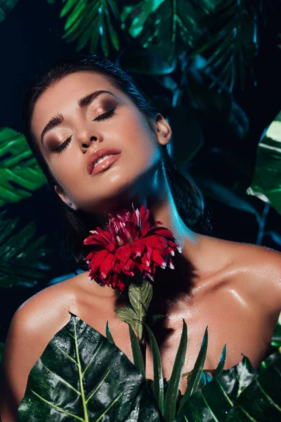 Young sexy woman holding red blooming flower near green leaves — Stock Photo